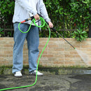 Person using a pressure washer with a green hose against a brick wall.