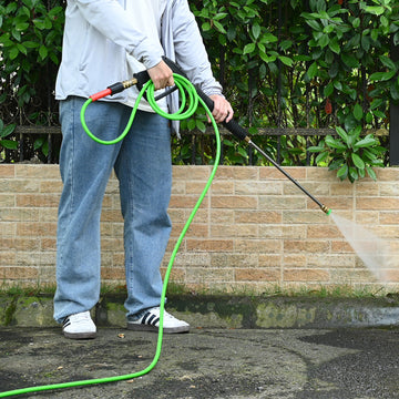 Person using a pressure washer with a green hose against a brick wall.