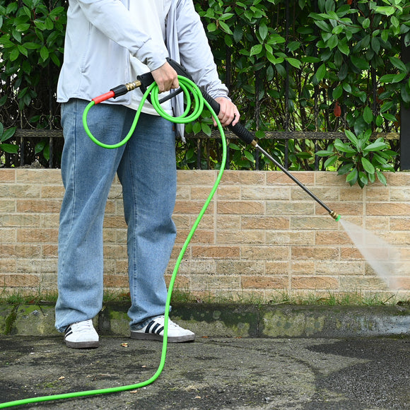 Person using a pressure washer with a green hose against a brick wall.